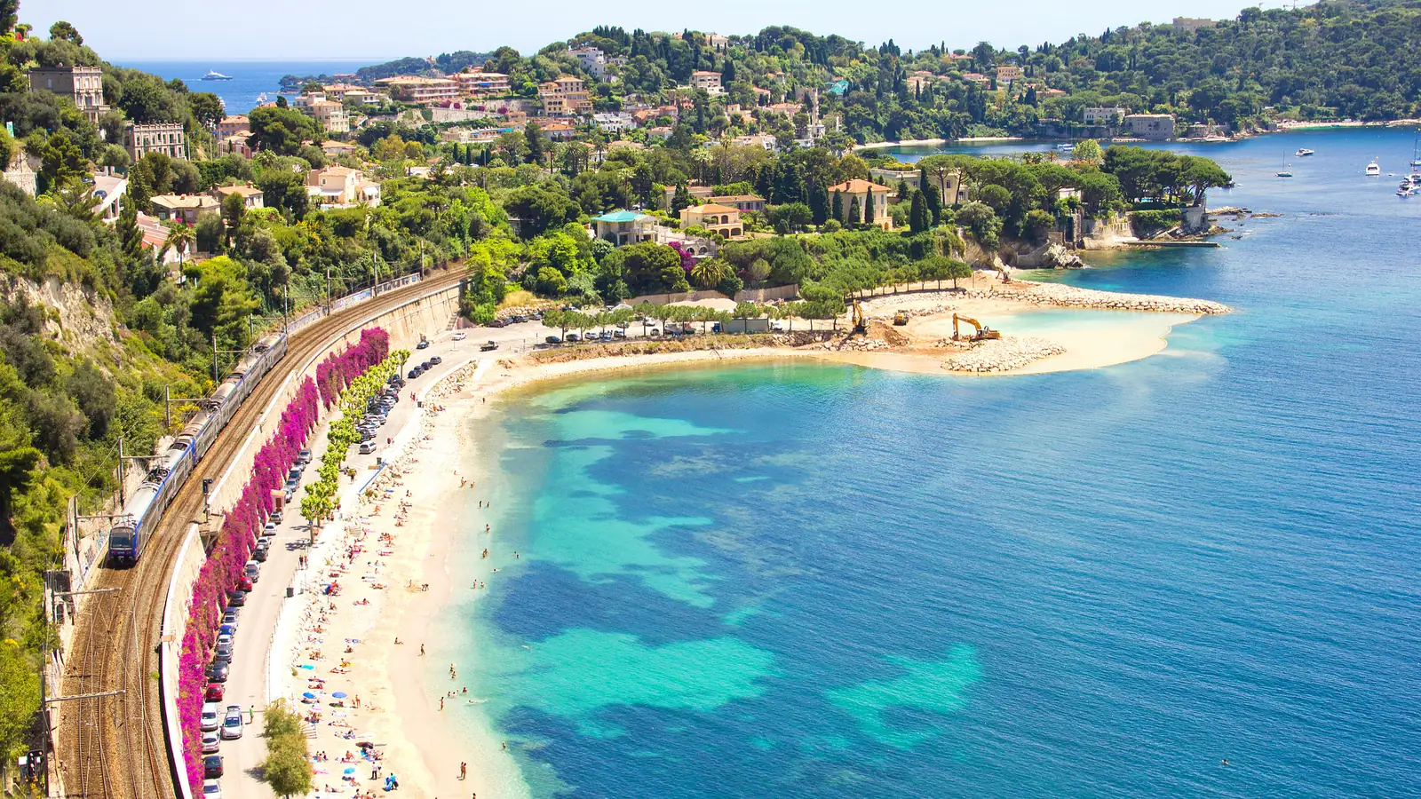A sandy beach and turquoise bay below hillside villas on the French Riviera