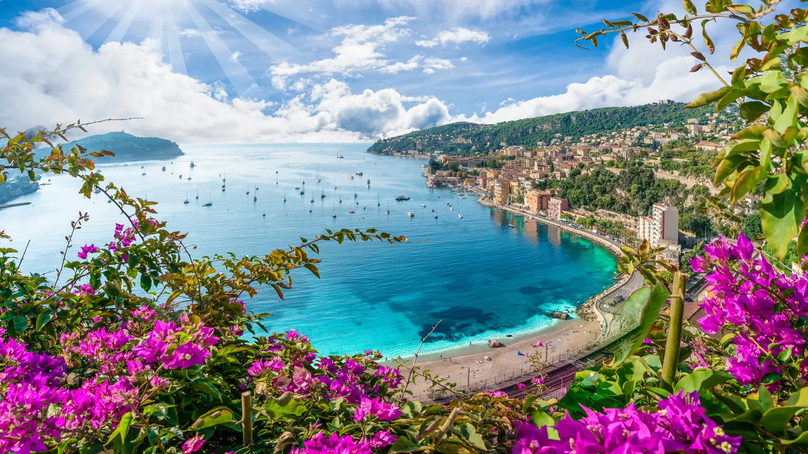 The bay of Villefranche-sur-Mer seen through bougainvillea, with yachts at anchor and the town along the shore