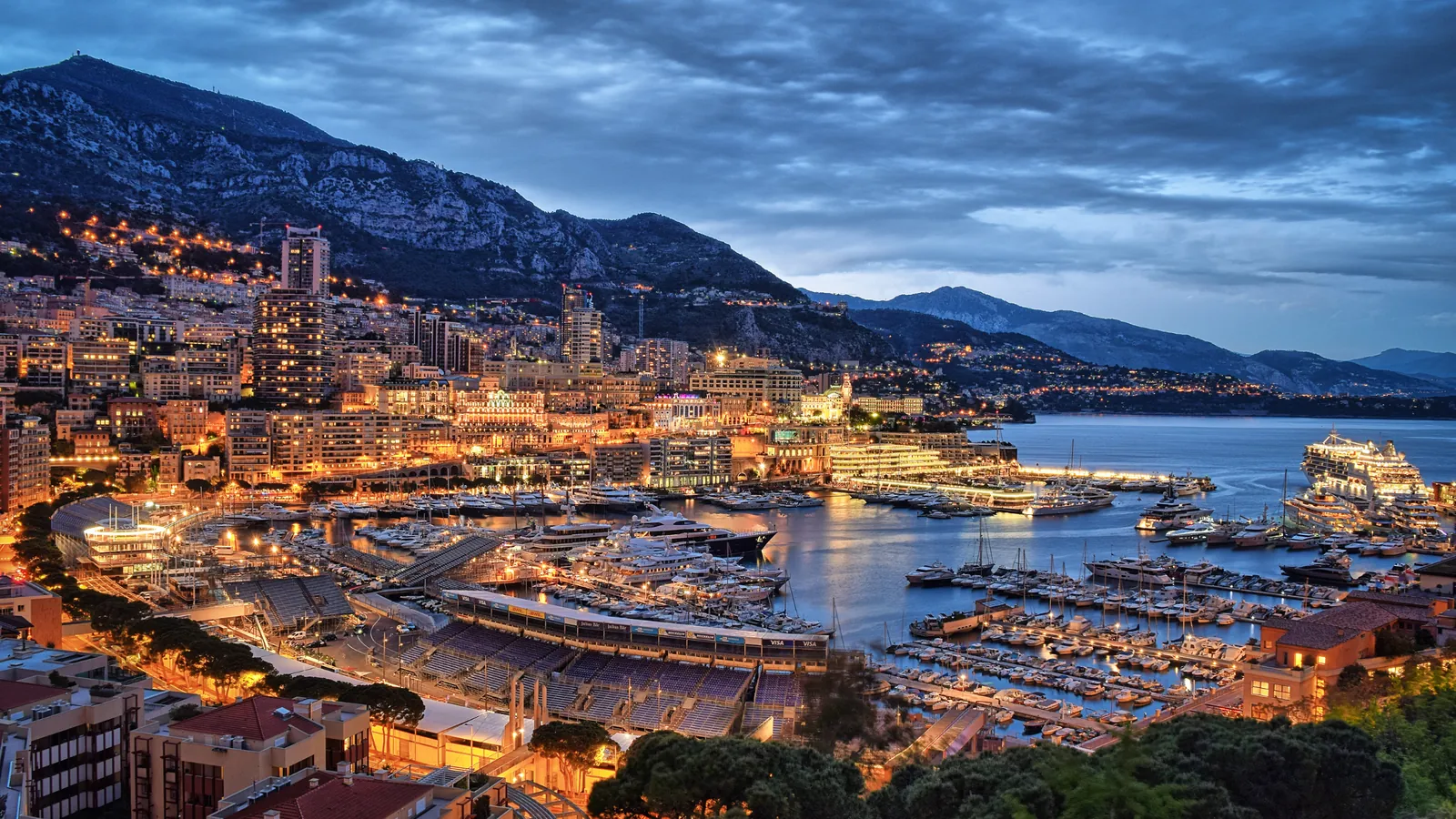 Monaco at dusk, with lights around Port Hercule and the mountains beyond