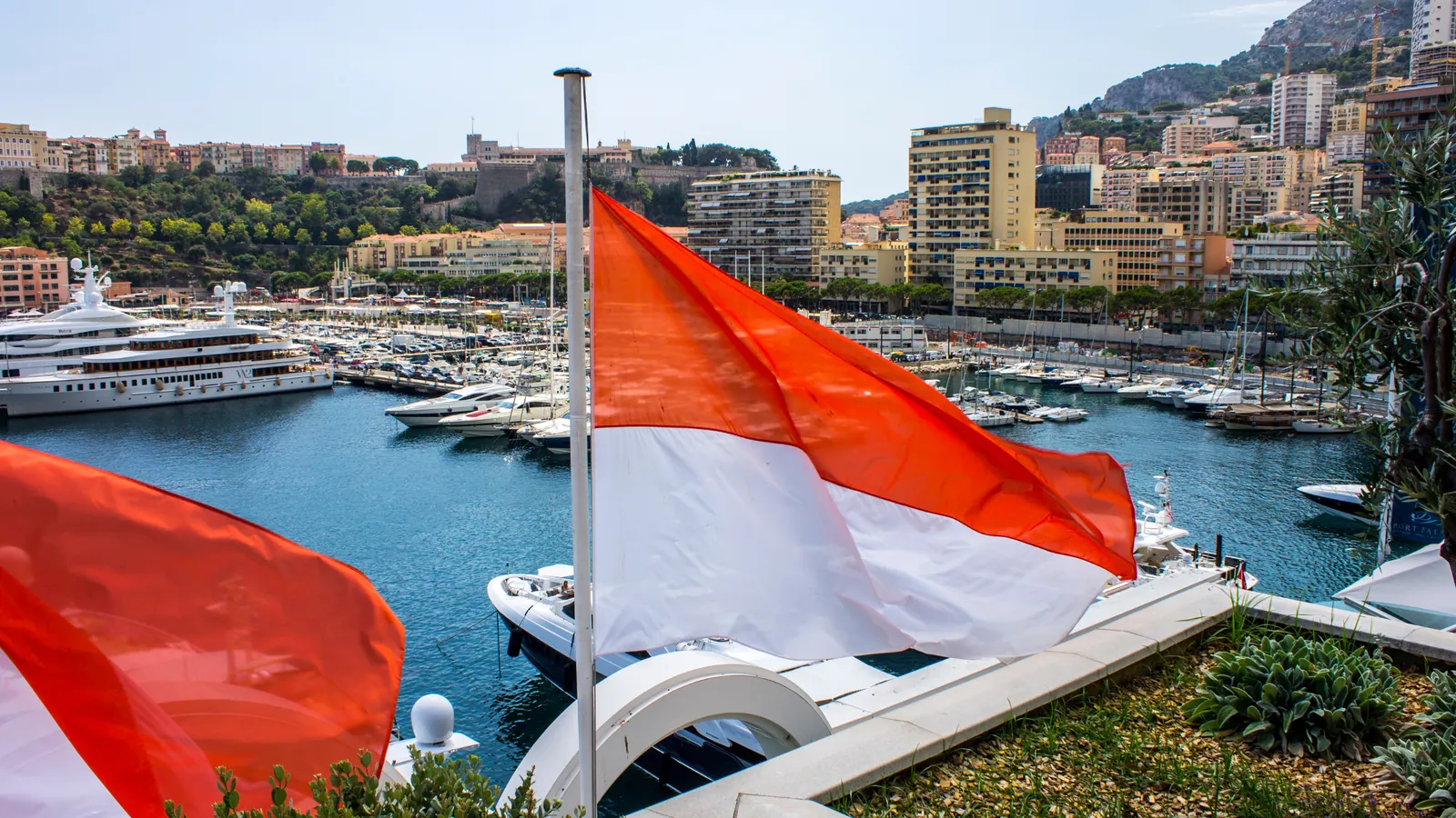 Monaco flags flying above Port Hercule, with the Rock and apartment buildings behind