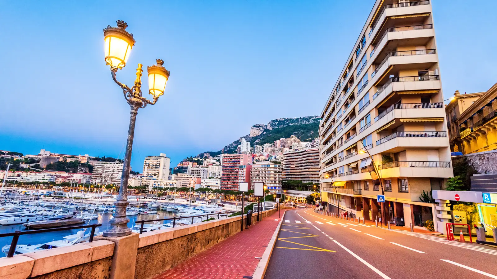 A harbor-side street in Monaco at dusk, with apartment buildings