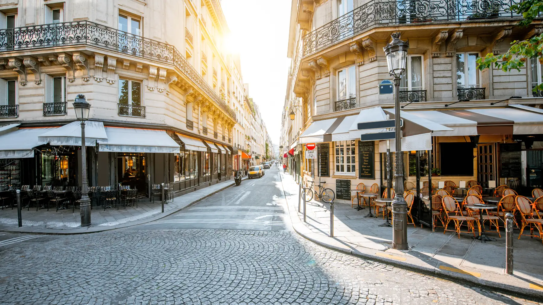 A Paris street corner with caf\xE9s and Haussmann apartment buildings in morning light