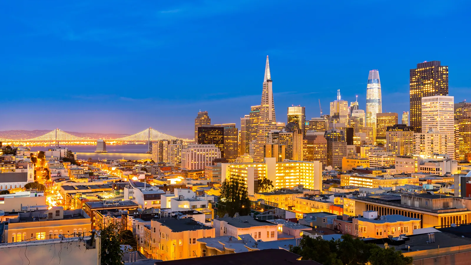 The San Francisco skyline and Bay Bridge at dusk, with city lights below
